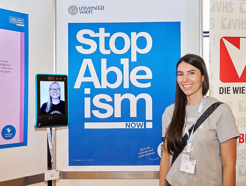 Rahel More und Michaela Joch vor dem Poster bei der LNF. Michaela Joch nutzt den Telepräsenzroboter der VHS.