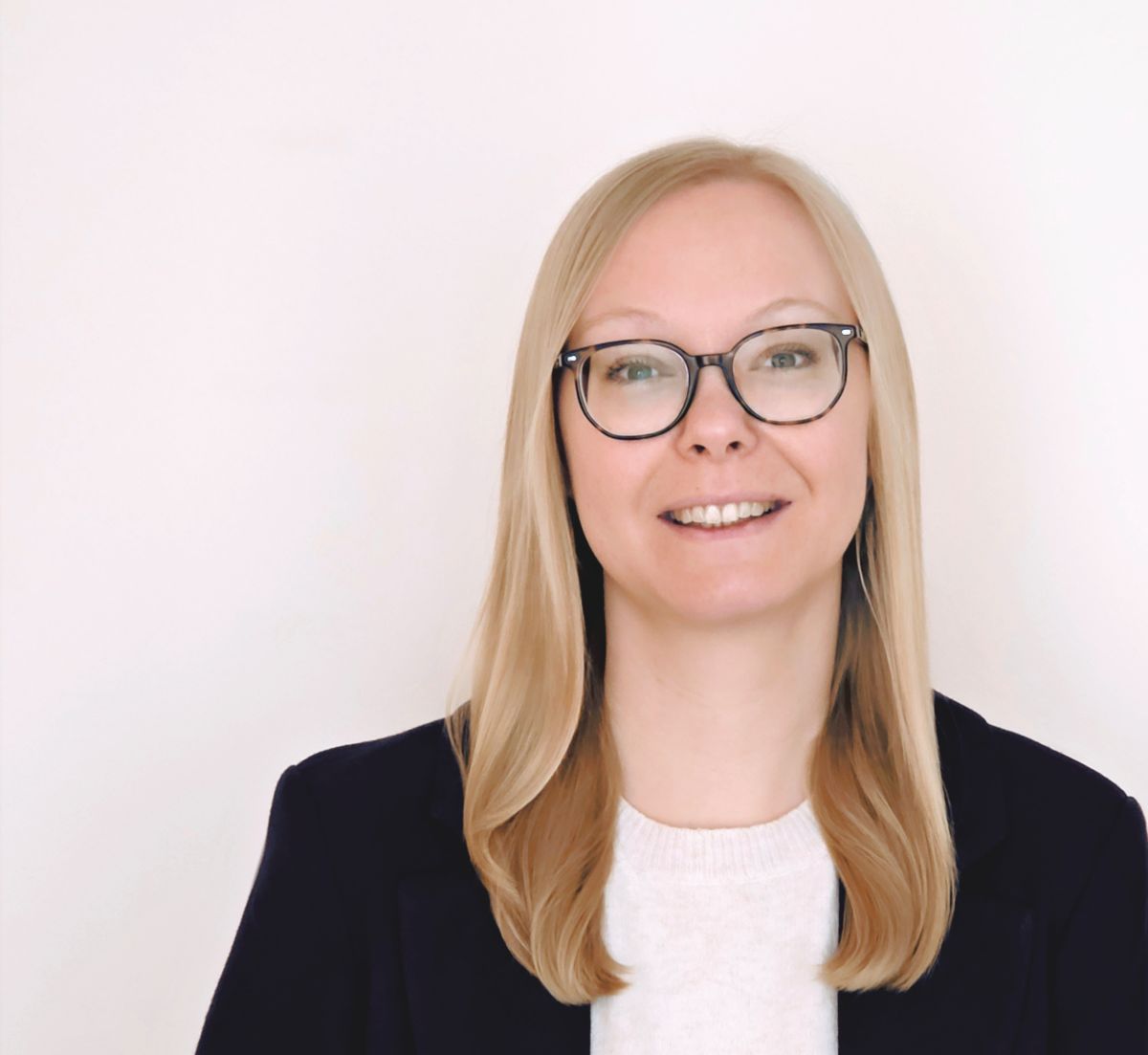 Michaela Joch ist eine weiße Frau Mitte 30, mit blonden 
langen Haaren und blauen Augen. Sie trägt eine Brille, eine hellblaue Bluse und darüber einen lila Pullover. Das
Foto ist vor einer Betonwand aufgenommen.